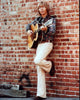 John Denver playing guitar leaning on a brick wall photo print.