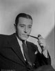 George Raft wearing a black coat and tie holding a tobacco pipe photo print.