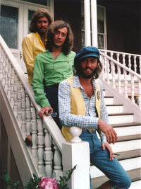 Bee Gees band group photo on white staircase in colorful shirts.
