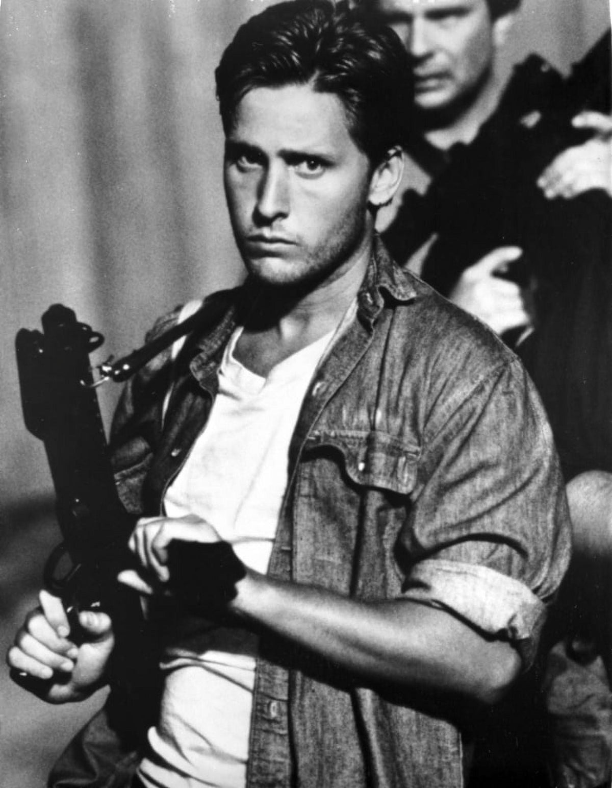 Photo print of Emilio Estevez wearing a denim jacket and carrying a gun.