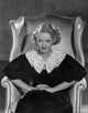 Bette Davis seated on a white leather couch in a black dress with white lace collar photo print.