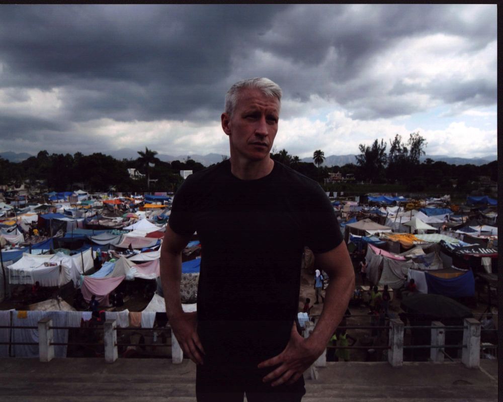 Photo print of Anderson Cooper with hands on hips in front of tent village.