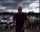 Photo print of Anderson Cooper with hands on hips in front of tent village.