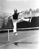 Fred Astaire jumping over a tennis net in a classic black and white photo print.