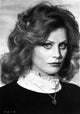Beverly D'Angelo close-up portrait in black dress with heart pendant necklace.
