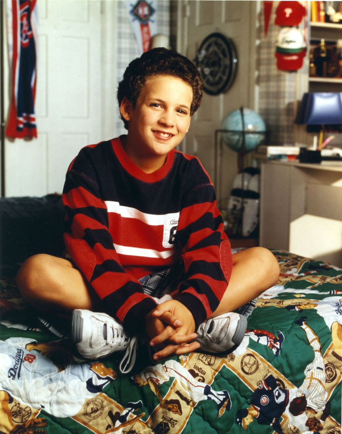 Ben Savage seated on printed bed in red long sleeve ringer shirt and white rubber shoes photo print.