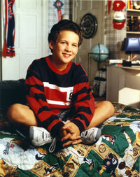Ben Savage seated on printed bed in red long sleeve ringer shirt and white rubber shoes photo print.