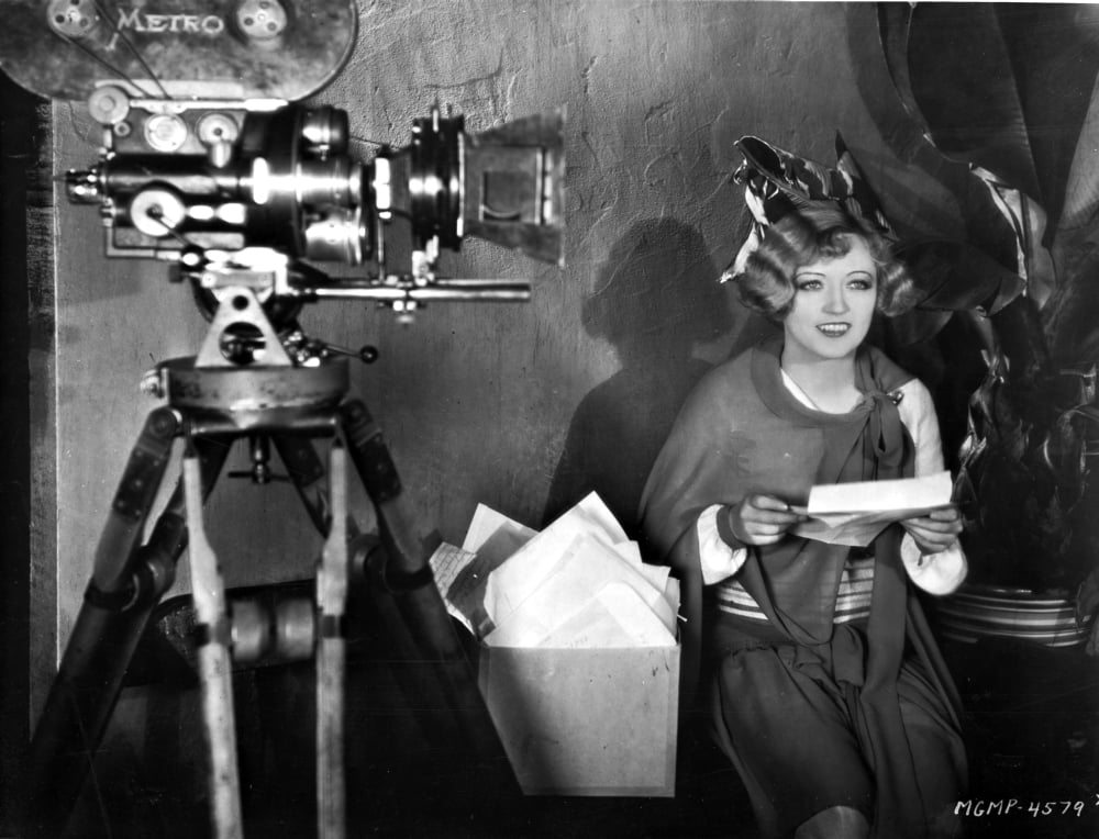 Black and white photo print of Marion Davies beside a camera.