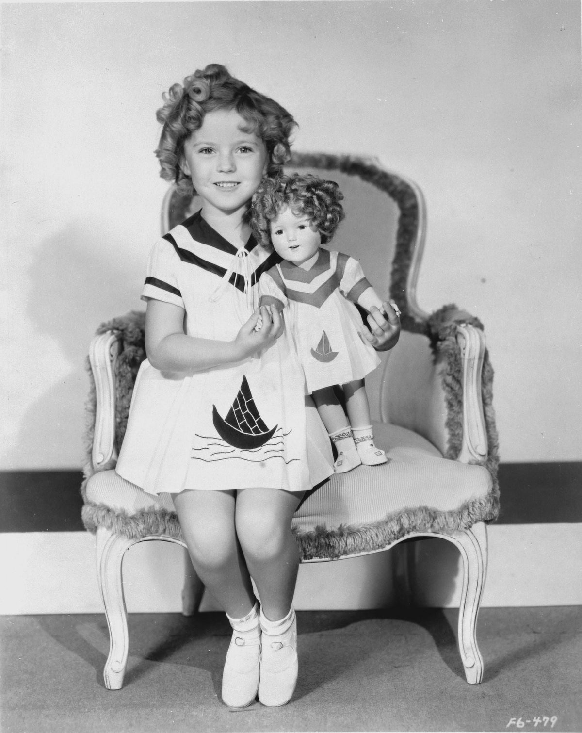 Shirley Temple sitting on a chair with doll in a white dress photo print