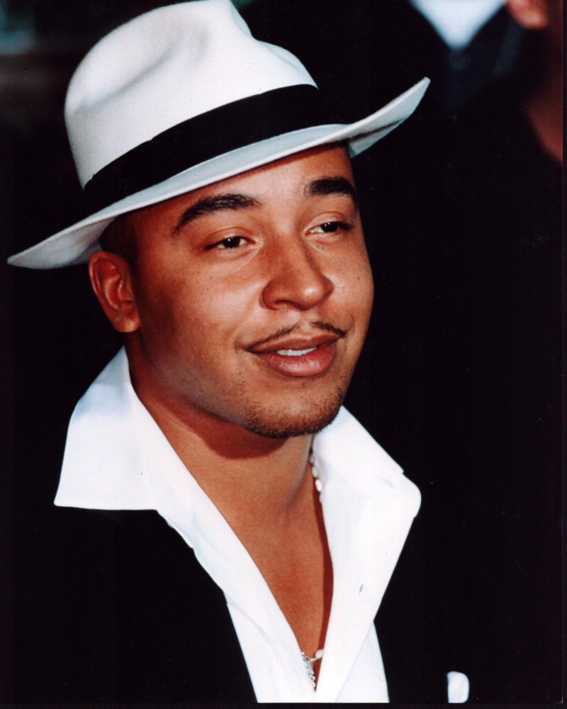 Lou Bega photo print in white fedora and unbuttoned shirt.
