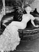 Mae West sitting on couch in white gown with floral sleeves photo print.