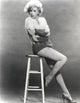Black and white photo print of Stella Stevens seated on stool wearing sweater top.
