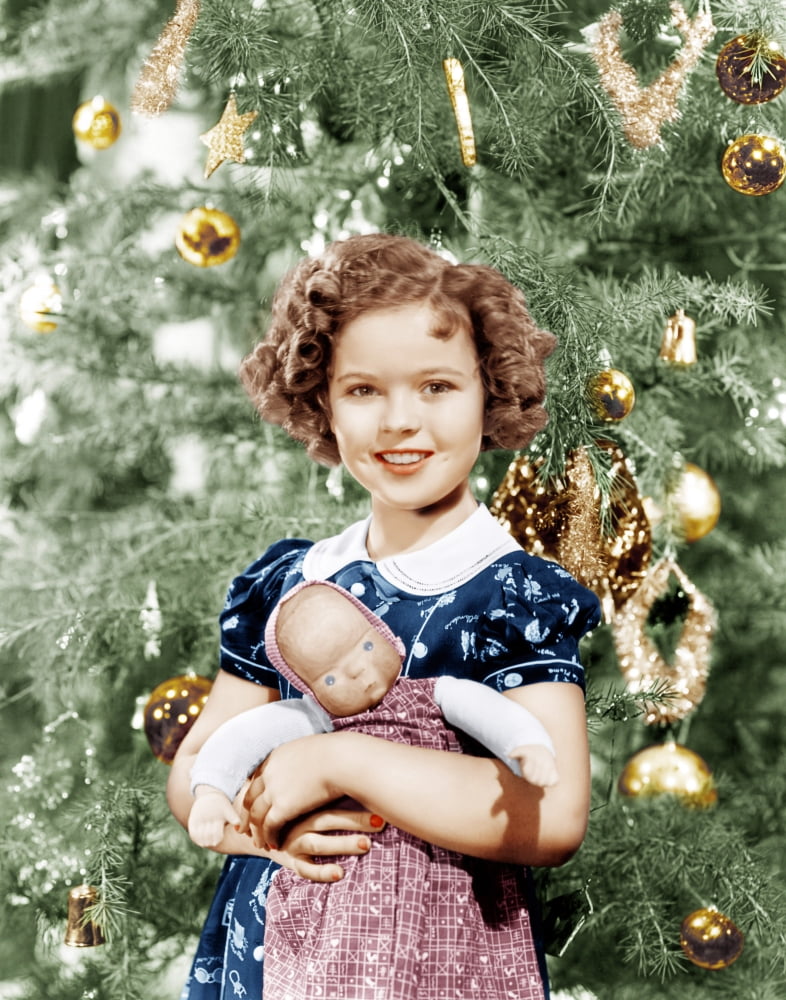 Vintage photo print of Shirley Temple holding a doll by the Christmas tree, late 1930s.