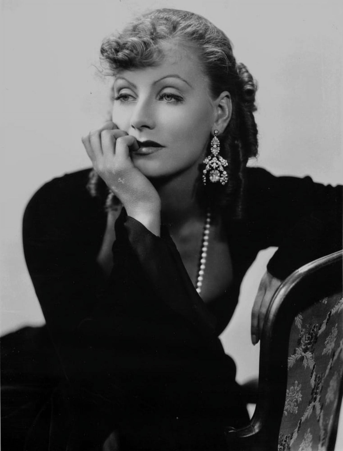 Greta Garbo photo print leaning on chair in black outfit.
