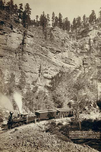 Two-car train poster print with passengers in front of a steep cliff.