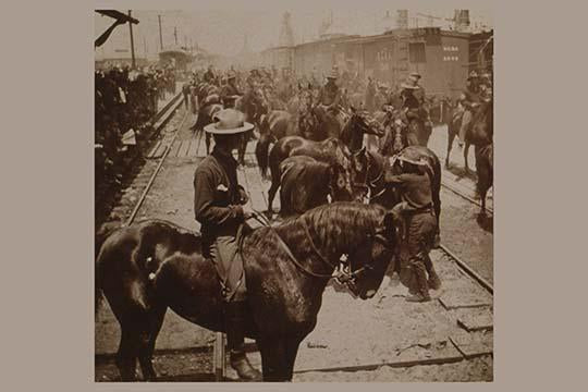 Poster print of a crowded scene with horses and riders disembarking from trains at Tampa.