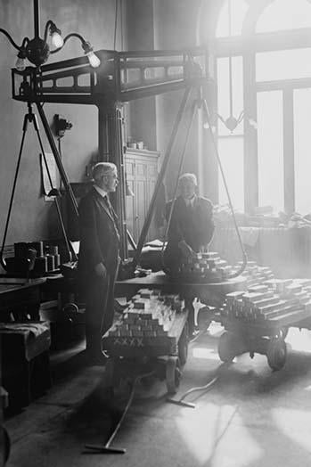 Two suited men weighing gold bars on scales at the US Mint poster print.