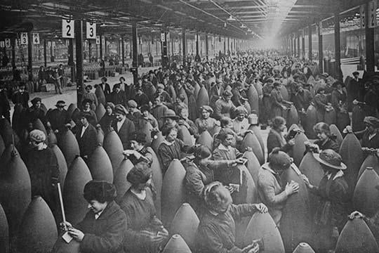 Throngs of women among large artillery shells on a factory floor poster print