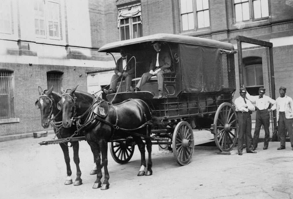 Horse-drawn wagon outside Bureau of Engraving and Printing building, featuring white wagon drivers and African American loaders.