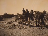 Three Navajos with horses gathered before a mound of rocks and vegetation.