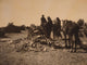 Three Navajos with horses gathered before a mound of rocks and vegetation.