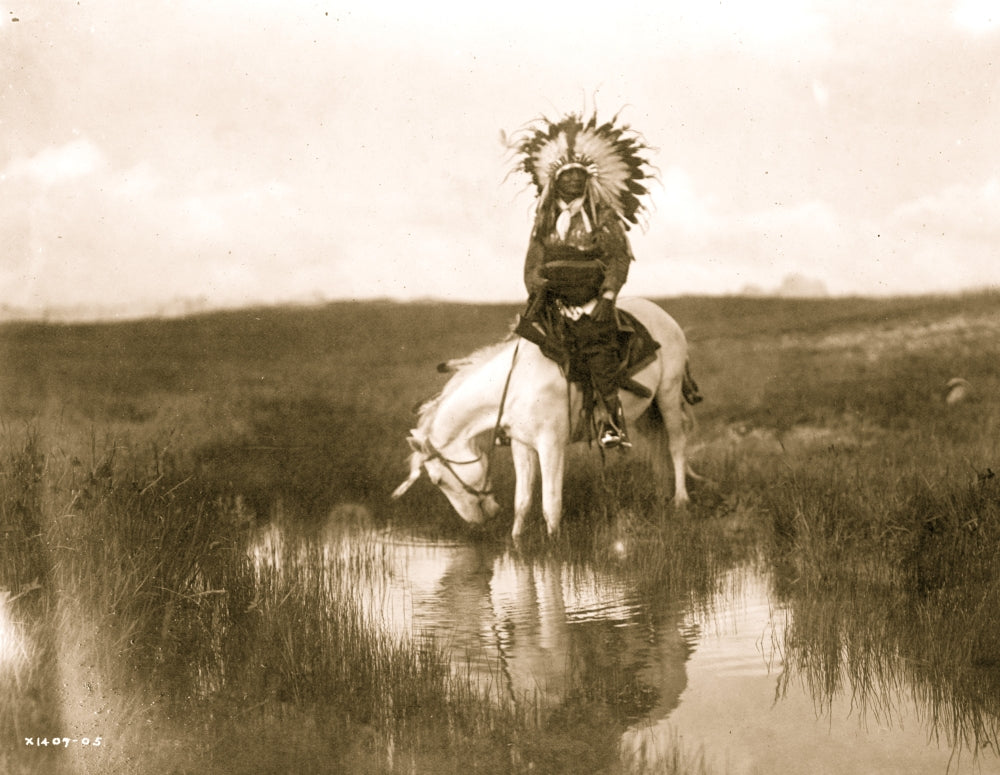 Cheyenne Indian wearing headdress riding a white stallion at a stream