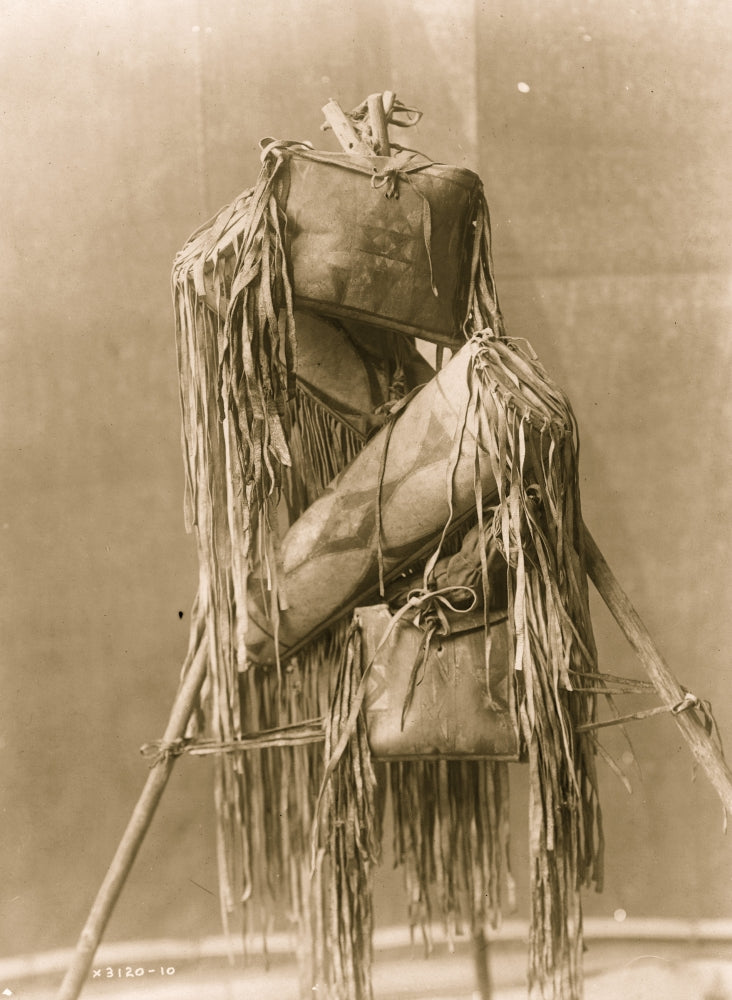 Four Piegan fringed leather containers displayed on a tripod