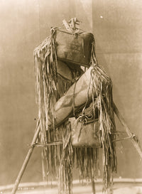 Four Piegan fringed leather containers displayed on a tripod