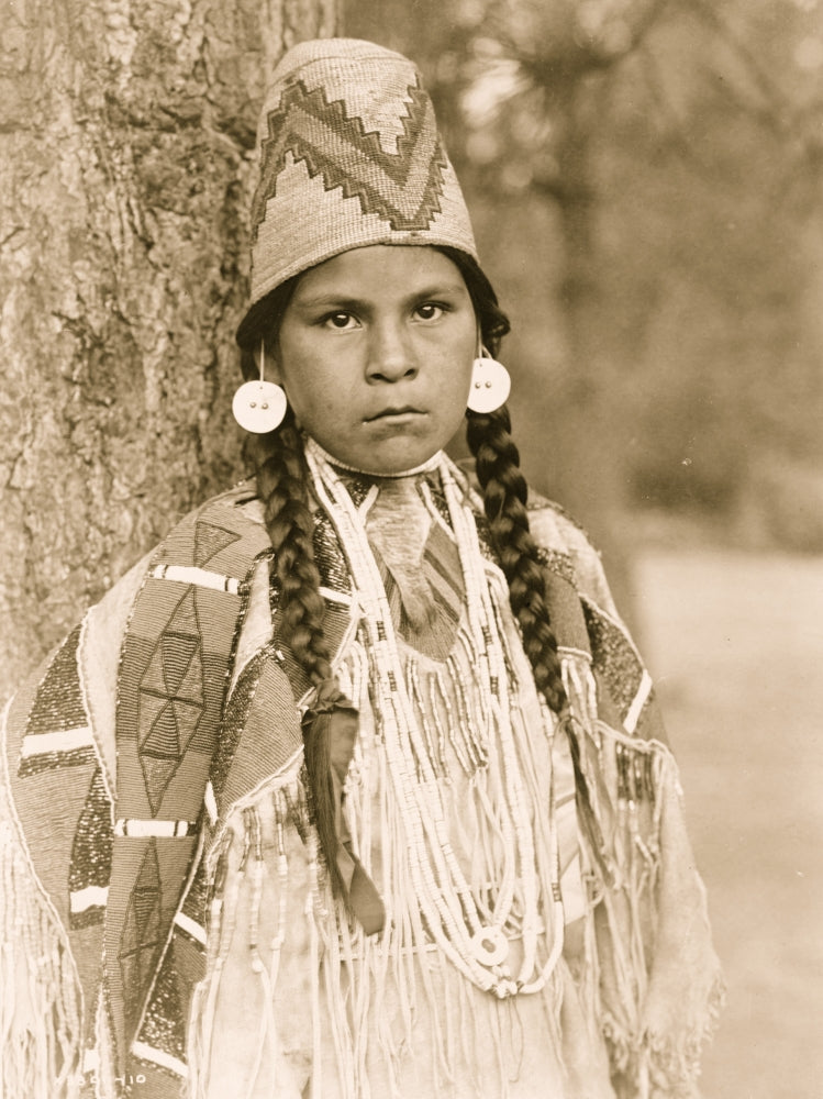 Umatilla woman half-length portrait standing in front of a tree, wearing traditional attire.