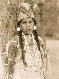 Umatilla woman half-length portrait standing in front of a tree, wearing traditional attire.