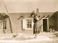 Tewa woman winnowing wheat in front of pueblo building poster print.