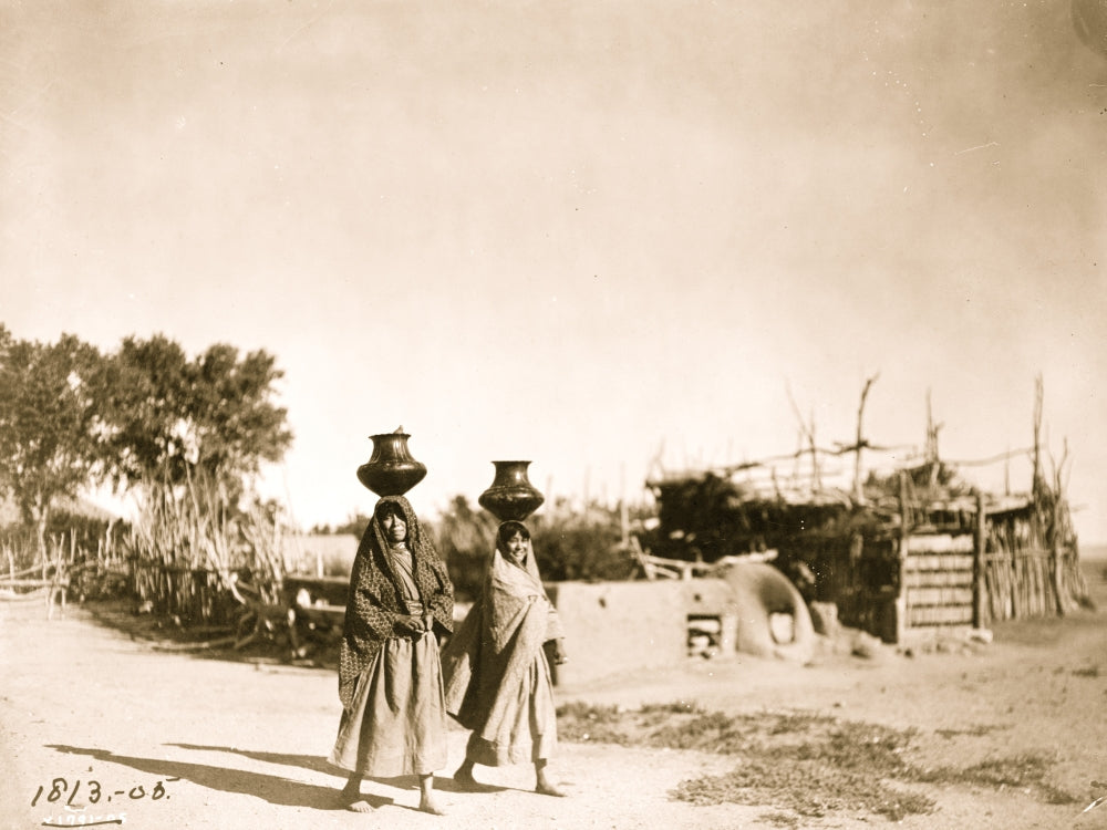 Two Pueblo women carrying jugs on their heads in a scenic desert landscape poster print.