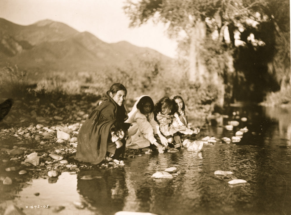 Four Taos children playing by a stream with mountains in the background.