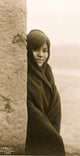 Three-quarter length portrait of a Zuni girl peering around a building.