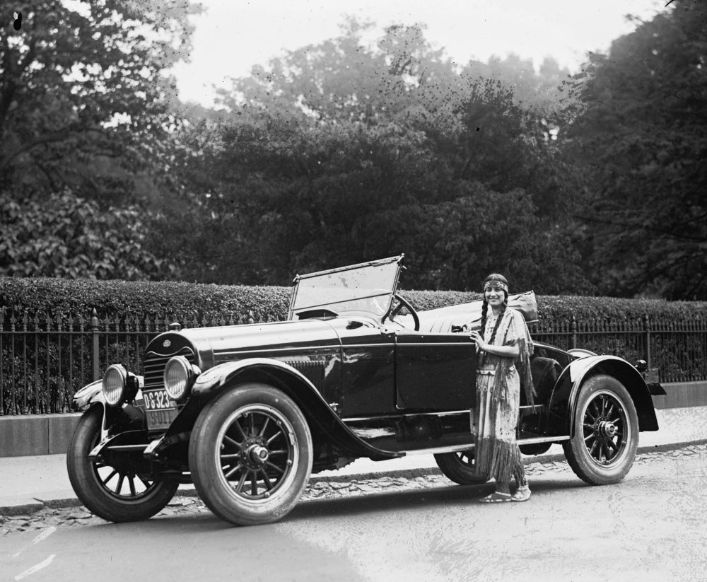 Woman in Native American clothing next to automobile poster print.