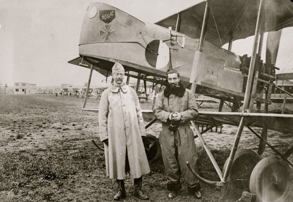 Capt. Berthaut and Capt. Hoppe in front of a German bi-plane poster print.