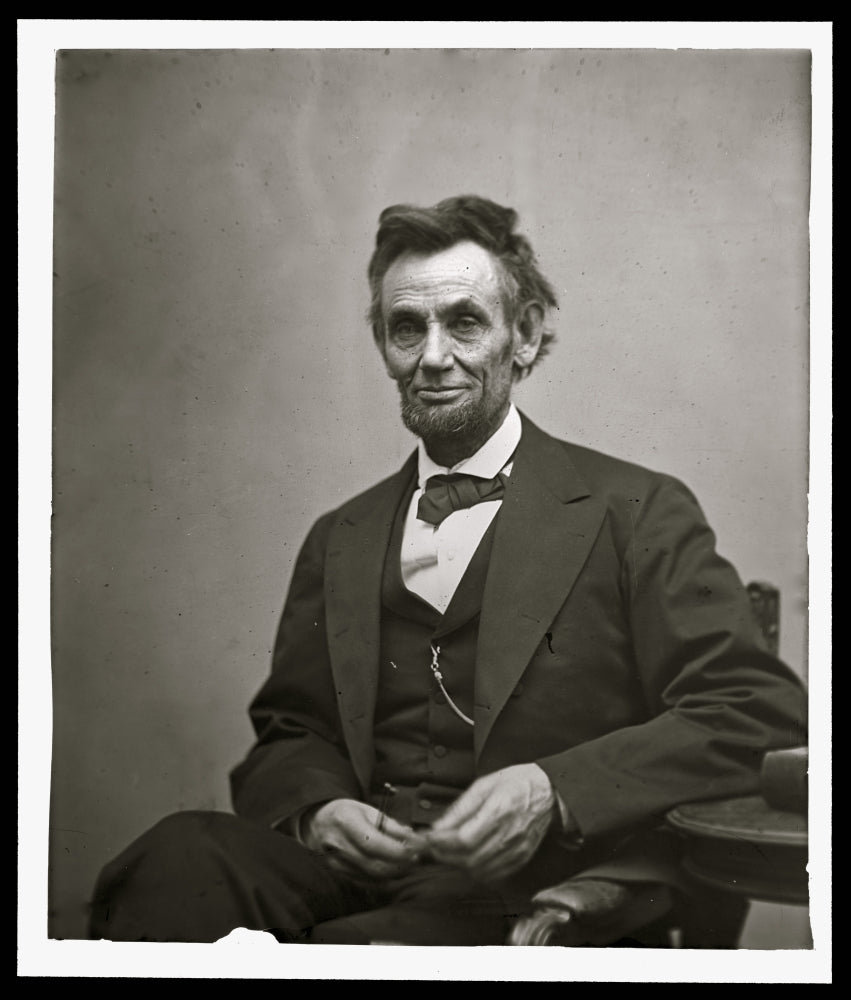 Abraham Lincoln three-quarter length portrait poster print showing him seated with spectacles and pencil.