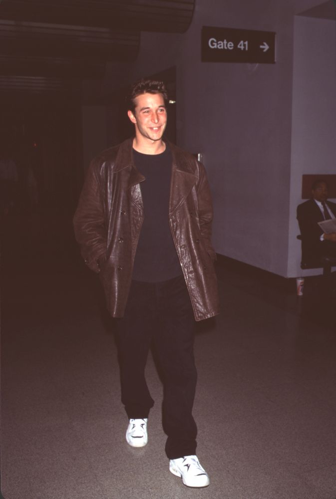 Noah Wyle photo print in black pants and brown leather jacket at LAX