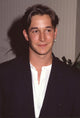 Noah Wyle closeup photo print in black jacket and unbuttoned white shirt.