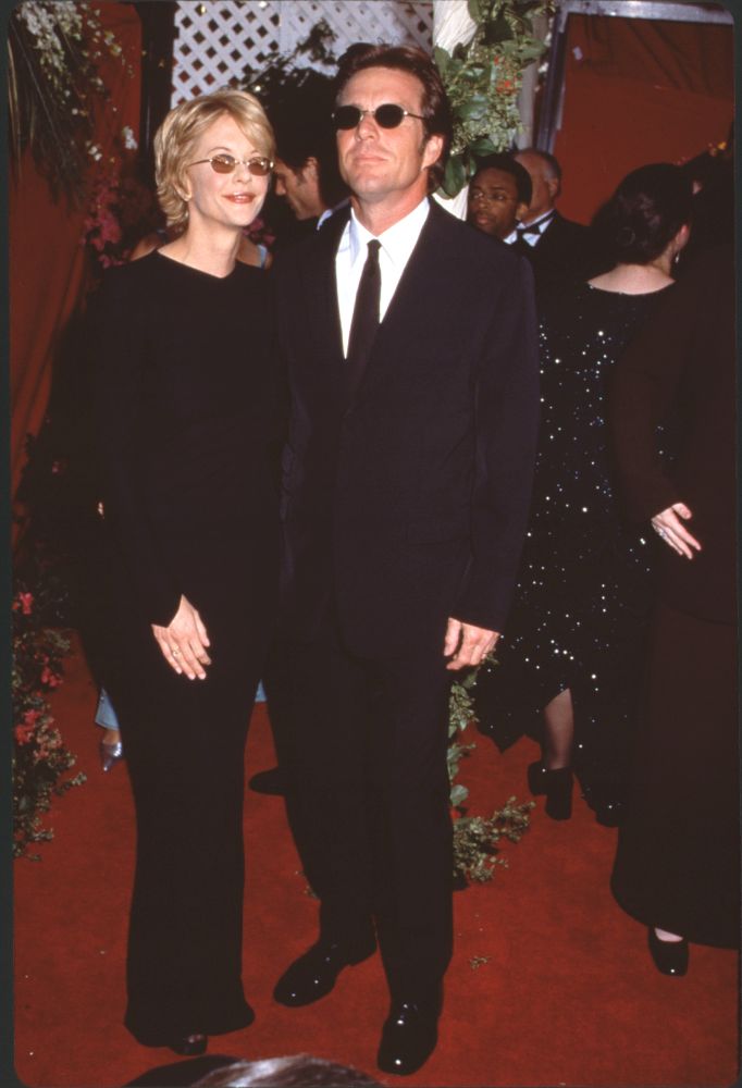 Meg Ryan in black long sleeves and brown sunglasses with Dennis Quaid at the 70th Academy Awards.