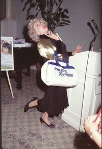 Phyllis Diller photo print in black dress with gold sleeves holding duffle bag