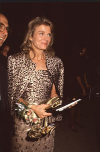 Candice Bergen fashion photo print holding gold shoes in animal print top and jacket.
