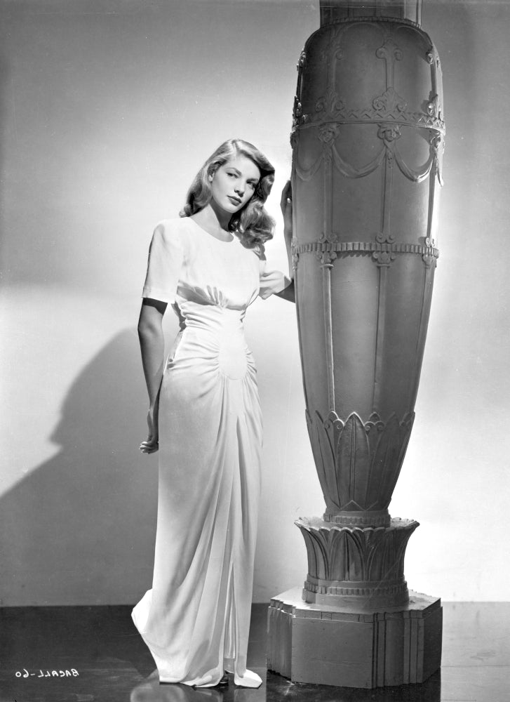 Lauren Bacall wearing a dress by a sculpture - Photo Print