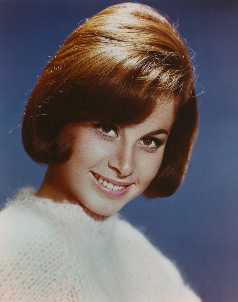 Close up portrait of Stefanie Powers smiling against a blue background.