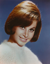 Close up portrait of Stefanie Powers smiling against a blue background.