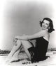 Jane Russell seated on the sand in a black one-piece swimsuit photo print.
