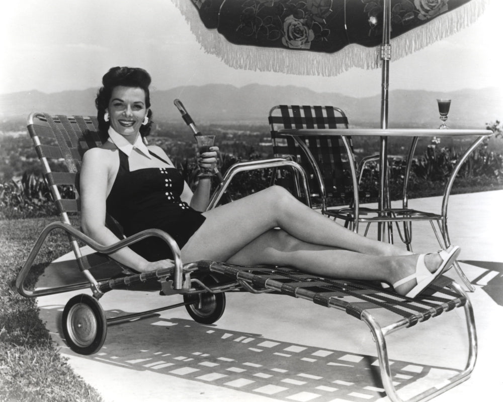 Jane Russell lying on a folding bed wearing a black dress, vintage photo print.