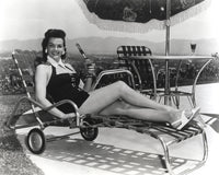 Jane Russell lying on a folding bed wearing a black dress, vintage photo print.
