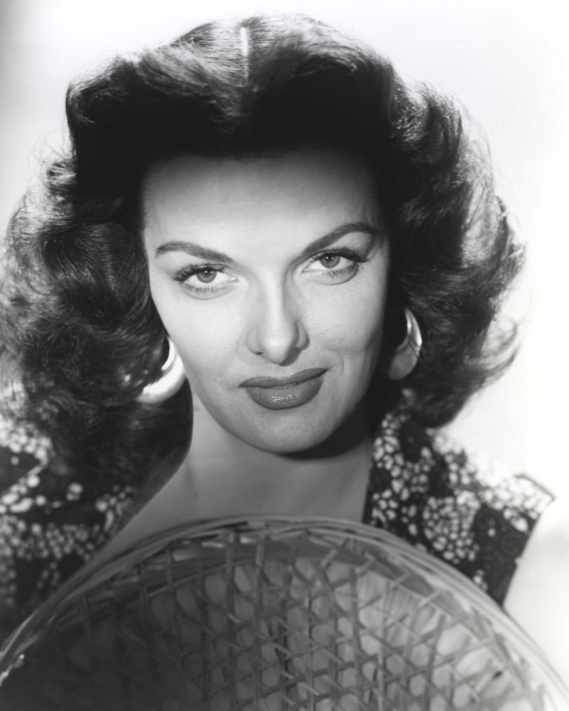 Jane Russell close-up portrait in black floral dress with straw hat on white background.