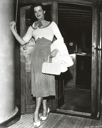 Jane Russell posed in a scoop-neck long sleeve dress with polka dot high waist skirt holding a white handbag.